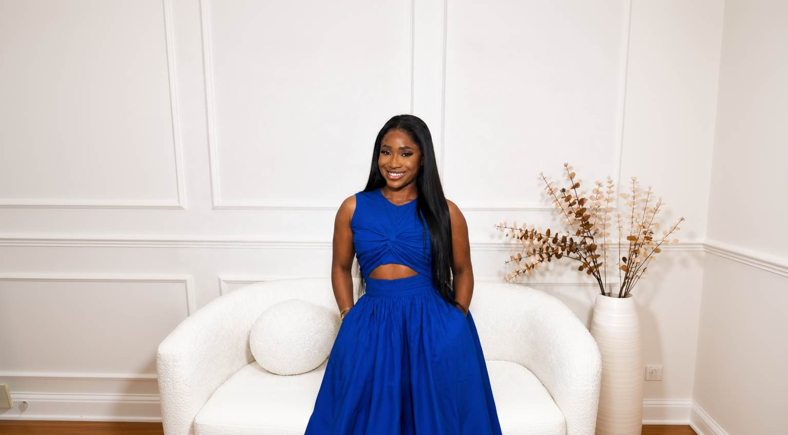 Woman in a blue dress standing in a room with white walls and furniture.
